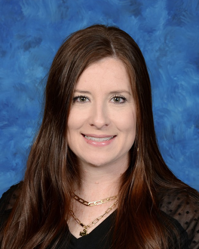 teacher with long brown hair smiles in front of a blue background